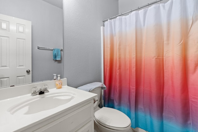 bathroom with a textured wall, vanity, curtained shower, and toilet