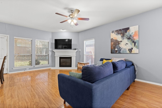 living room with a glass covered fireplace, light wood-type flooring, baseboards, and ceiling fan