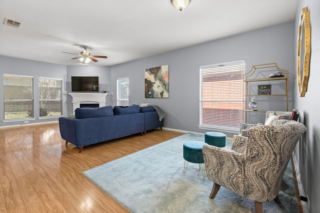 living area featuring wood finished floors, visible vents, a ceiling fan, and a healthy amount of sunlight