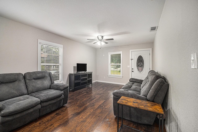 living area with a textured ceiling, ceiling fan, baseboards, dark wood-style flooring, and visible vents
