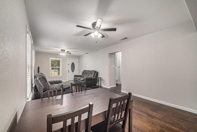 dining room with a textured wall, visible vents, a ceiling fan, baseboards, and dark wood-style flooring