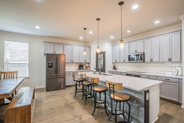 kitchen with light wood finished floors, stainless steel appliances, a sink, gray cabinetry, and a breakfast bar area