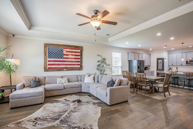 living area with wood finished floors, a tray ceiling, ceiling fan, and crown molding