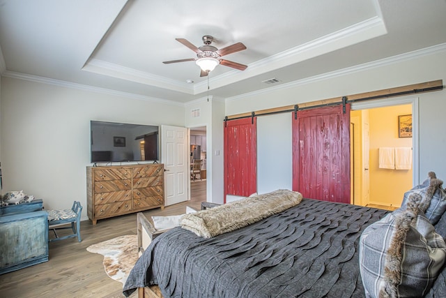 bedroom with a barn door, crown molding, wood finished floors, a tray ceiling, and visible vents