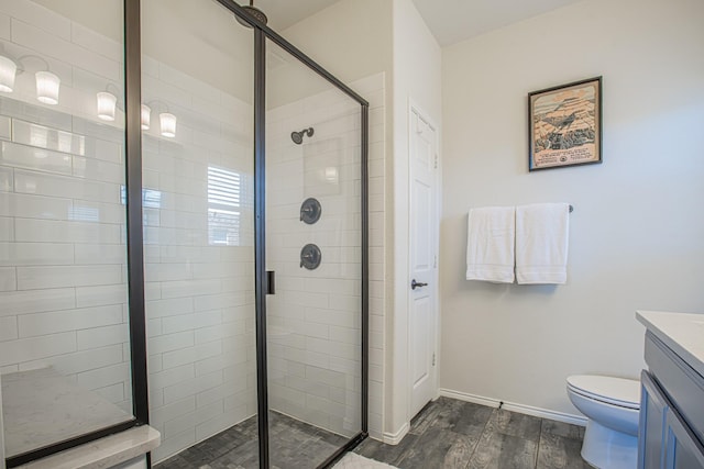 bathroom with toilet, a stall shower, baseboards, wood finished floors, and vanity