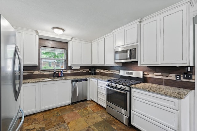 kitchen with decorative backsplash, white cabinets, a sink, stone finish flooring, and stainless steel appliances