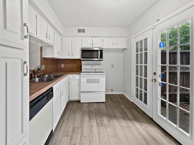 kitchen with light wood-style flooring, a textured ceiling, a sink, white cabinetry, and white appliances