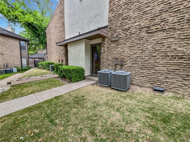 view of exterior entry with a lawn, central AC, stucco siding, and fence