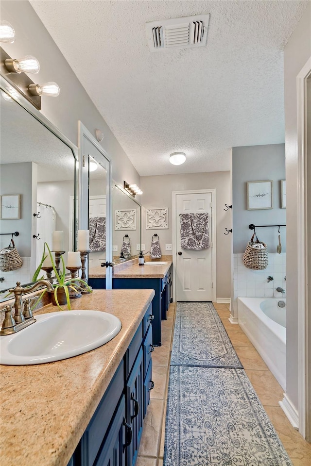 bathroom with a sink, a textured ceiling, a bath, two vanities, and visible vents