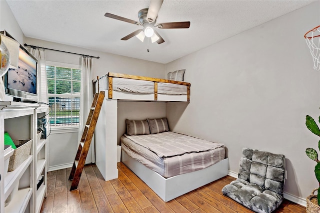 bedroom with wood-type flooring, a textured ceiling, a ceiling fan, and baseboards