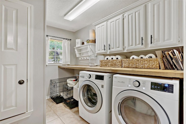 clothes washing area with a textured ceiling, light tile patterned floors, cabinet space, washing machine and dryer, and baseboards