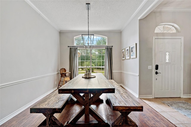dining space featuring light wood-style flooring, a textured ceiling, baseboards, an inviting chandelier, and ornamental molding