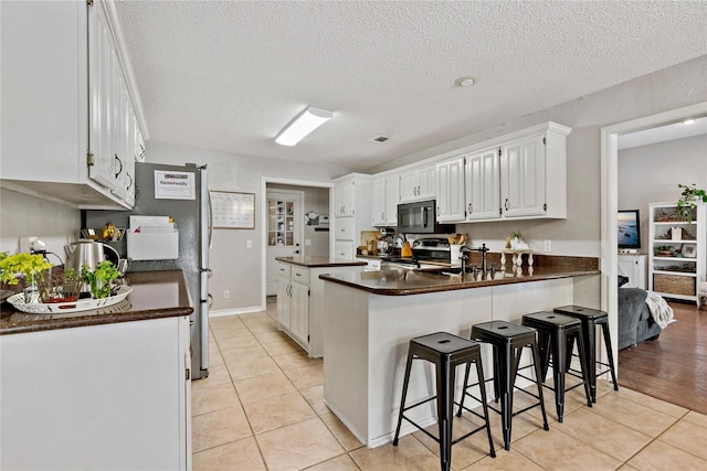kitchen with a peninsula, stainless steel electric range oven, dark countertops, black microwave, and light tile patterned floors