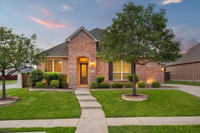 traditional home with brick siding, roof with shingles, a front yard, and fence