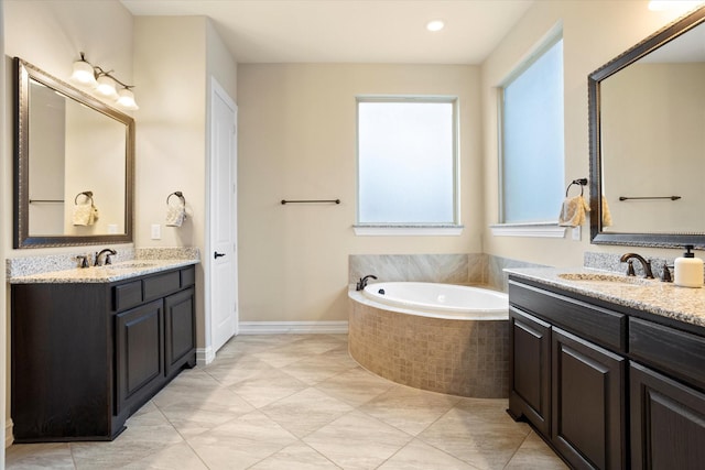 full bathroom featuring a bath, baseboards, a sink, and two vanities