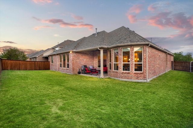 rear view of house featuring roof with shingles, a fenced backyard, brick siding, a lawn, and a patio