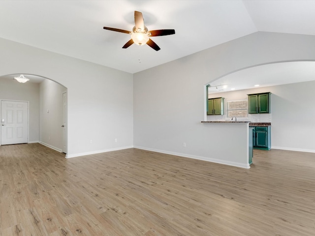 unfurnished living room with arched walkways, a ceiling fan, light wood finished floors, and baseboards