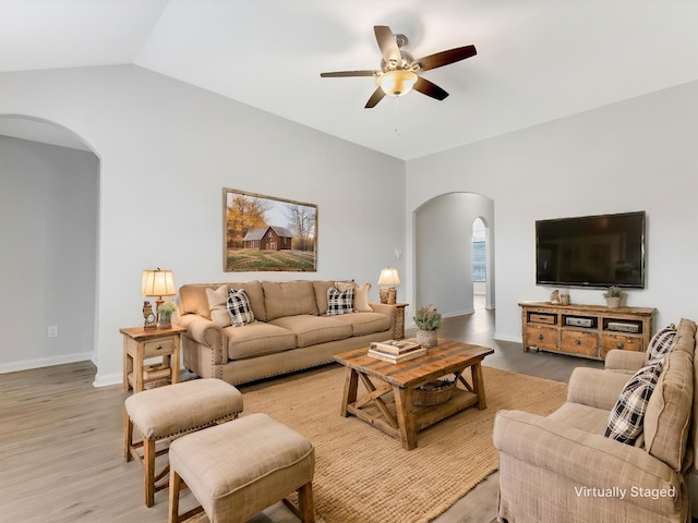 living area featuring arched walkways, light wood-type flooring, vaulted ceiling, baseboards, and a ceiling fan