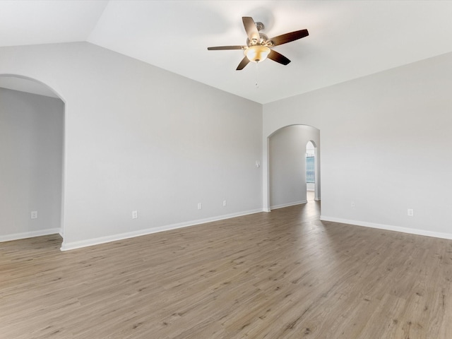 spare room with lofted ceiling, arched walkways, baseboards, light wood-style flooring, and ceiling fan