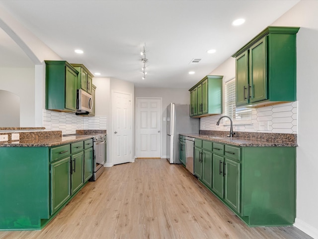 kitchen with arched walkways, appliances with stainless steel finishes, a sink, and light wood-style flooring