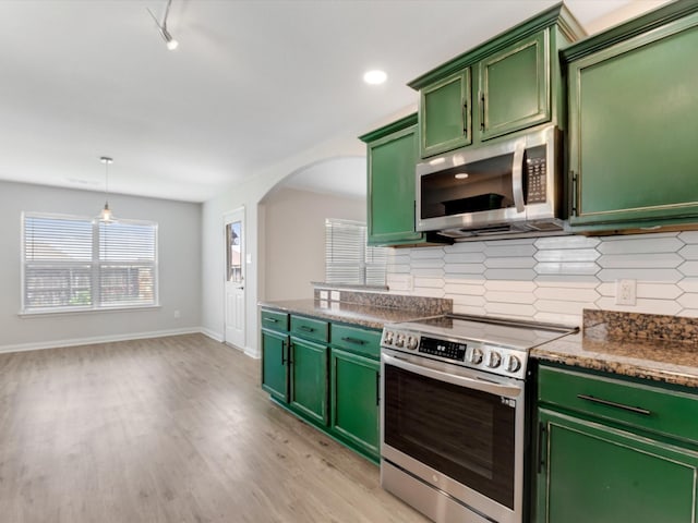 kitchen featuring light wood finished floors, dark countertops, decorative backsplash, green cabinets, and appliances with stainless steel finishes
