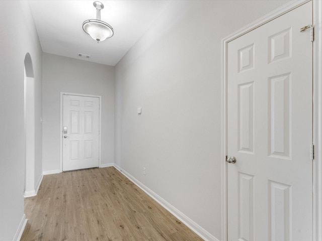 corridor featuring baseboards, arched walkways, visible vents, and light wood-type flooring