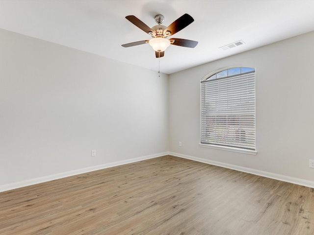 spare room featuring light wood finished floors, baseboards, visible vents, and ceiling fan