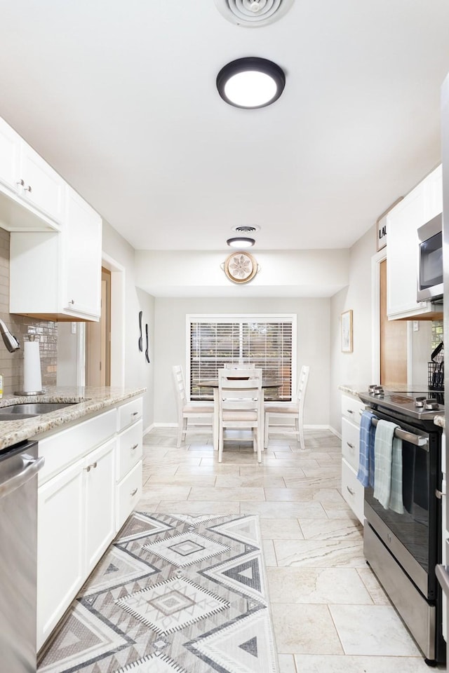kitchen featuring stainless steel appliances, a sink, backsplash, and white cabinetry