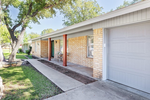 doorway to property featuring brick siding, a yard, a garage, and covered porch