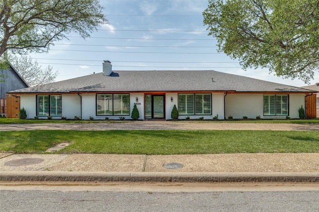 ranch-style home with a shingled roof, a chimney, brick siding, and a front lawn