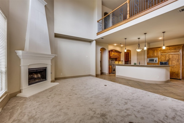 4312 Blue Quail Dr, Mckinney, TX 75072 - unfurnished living room with light carpet, arched walkways, a large fireplace, light tile patterned floors, and a towering ceiling