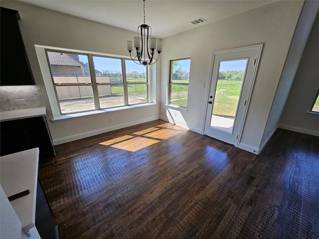 unfurnished dining area featuring an inviting chandelier, a healthy amount of sunlight, wood finished floors, and visible vents