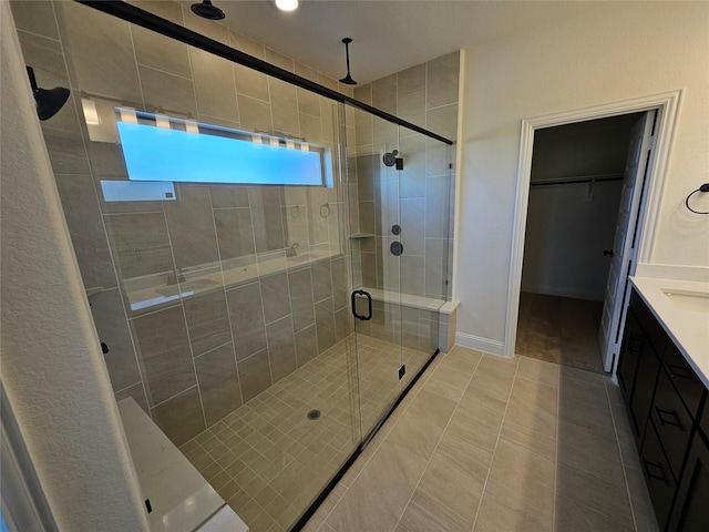 full bath featuring a shower stall, tile patterned floors, vanity, a walk in closet, and baseboards