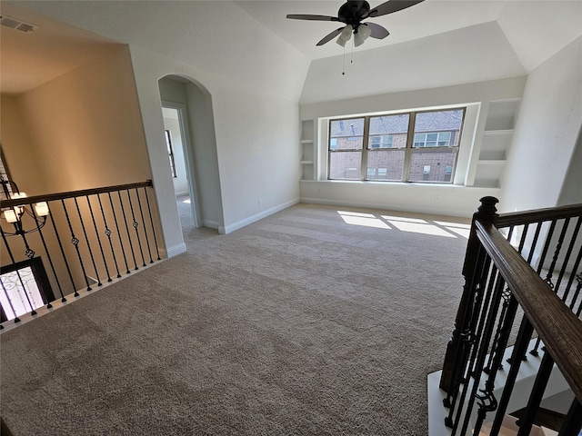spare room with light colored carpet, arched walkways, baseboards, built in shelves, and ceiling fan