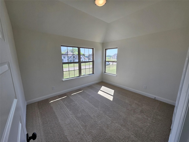 spare room featuring lofted ceiling, baseboards, and dark carpet