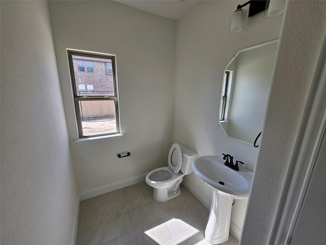 half bathroom with baseboards, toilet, tile patterned floors, and a sink