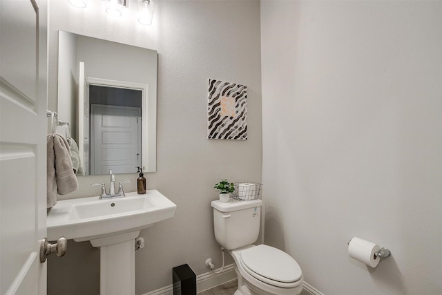 half bath featuring baseboards and toilet