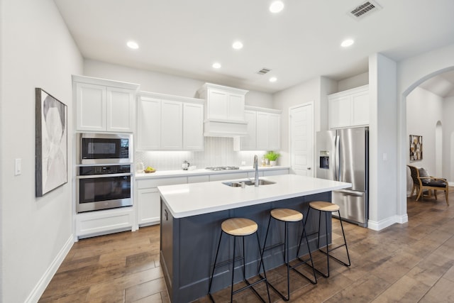 8517 Holliday Creek Way, Mckinney, TX 75071 - kitchen featuring appliances with stainless steel finishes, arched walkways, a sink, dark wood-type flooring, and a center island with sink