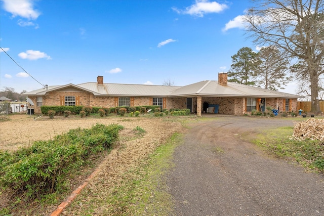 single story home with brick siding, dirt driveway, a chimney, and an attached carport