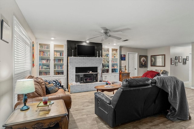 living room featuring visible vents, built in features, a ceiling fan, wood finished floors, and a brick fireplace