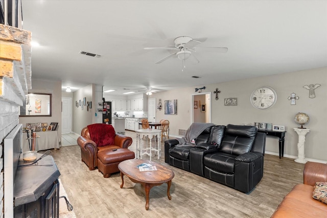 living room featuring a stone fireplace, visible vents, a ceiling fan, light wood-type flooring, and baseboards