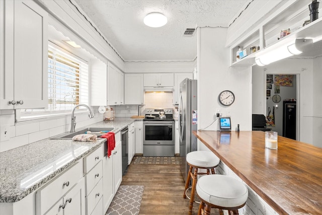 kitchen with under cabinet range hood, stainless steel appliances, visible vents, a sink, and a textured ceiling