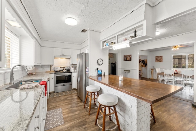 kitchen with a sink, dark wood-type flooring, a textured ceiling, appliances with stainless steel finishes, and white cabinetry