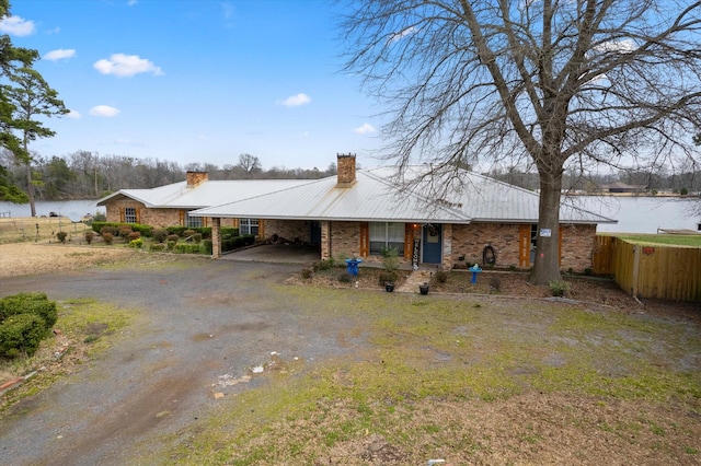 view of front of home with dirt driveway, a chimney, fence, a water view, and metal roof