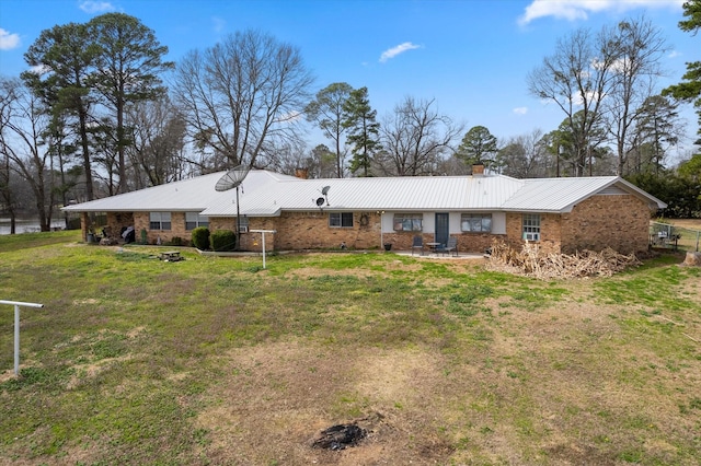 rear view of house featuring a chimney, metal roof, brick siding, a patio area, and a lawn