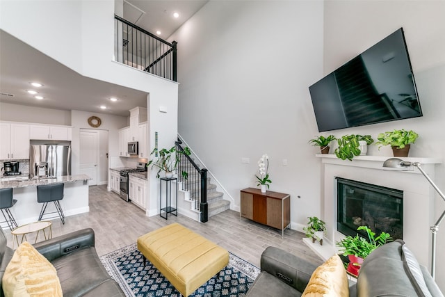 living area with stairway, a high ceiling, light wood finished floors, baseboards, and a glass covered fireplace