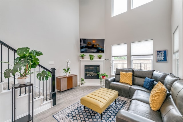 living room featuring a glass covered fireplace, wood finished floors, a high ceiling, and stairway