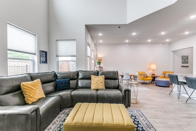 living room with recessed lighting, a towering ceiling, visible vents, and light wood-type flooring