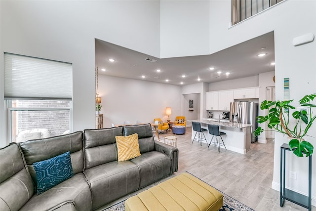living room with recessed lighting, light wood-type flooring, visible vents, and a towering ceiling