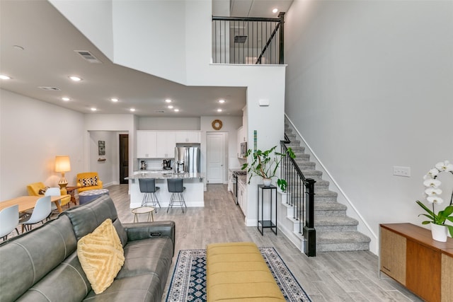 living room featuring stairs, visible vents, a high ceiling, and light wood-style floors